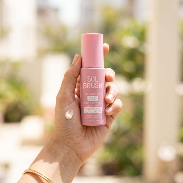 Hand holding the Tinted SPF Moisturizer bottle with a small drop of the tinted cream on the skin