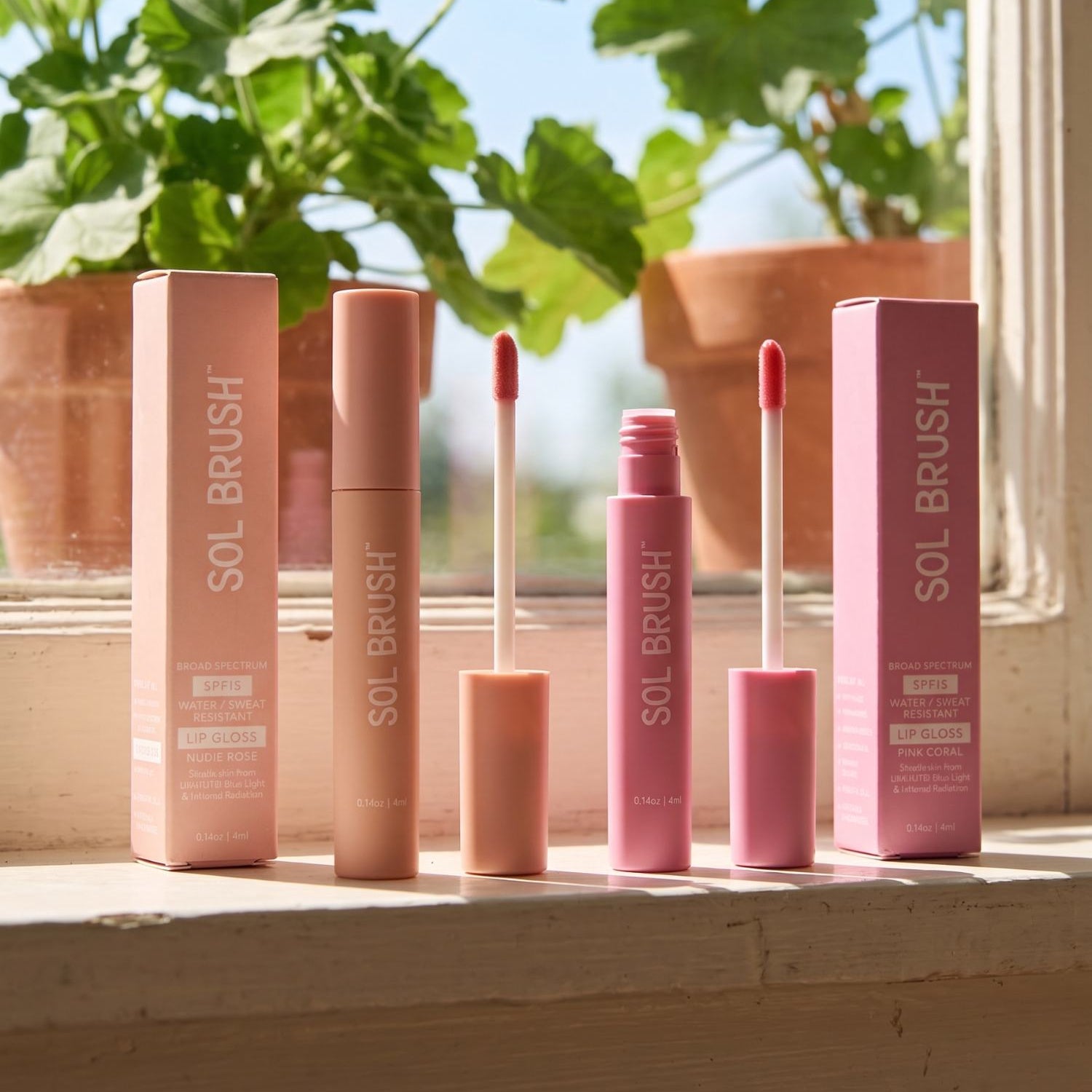 Two Sol Brush SPF 15 lip glosses in nude and pink with applicator wands and boxes on a sunny windowsill
