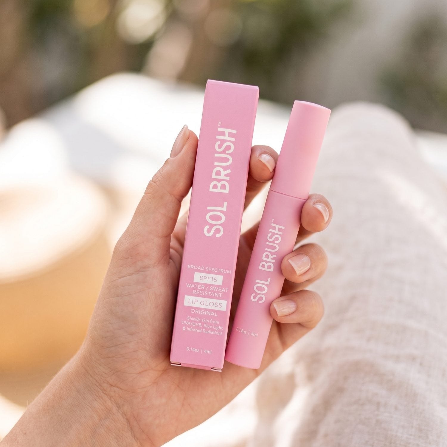 Hand holding the pink Sol Brush Broad Spectrum SPF 15 Lip Gloss tube and its box