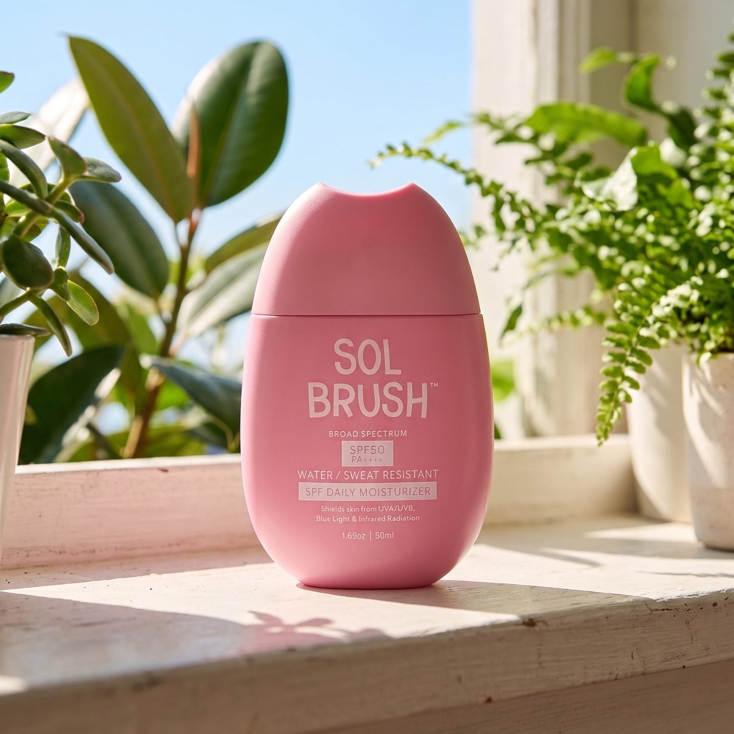 Pink Daily Moisturizer Broad Spectrum SPF 50 bottle on a sunny windowsill surrounded by houseplants