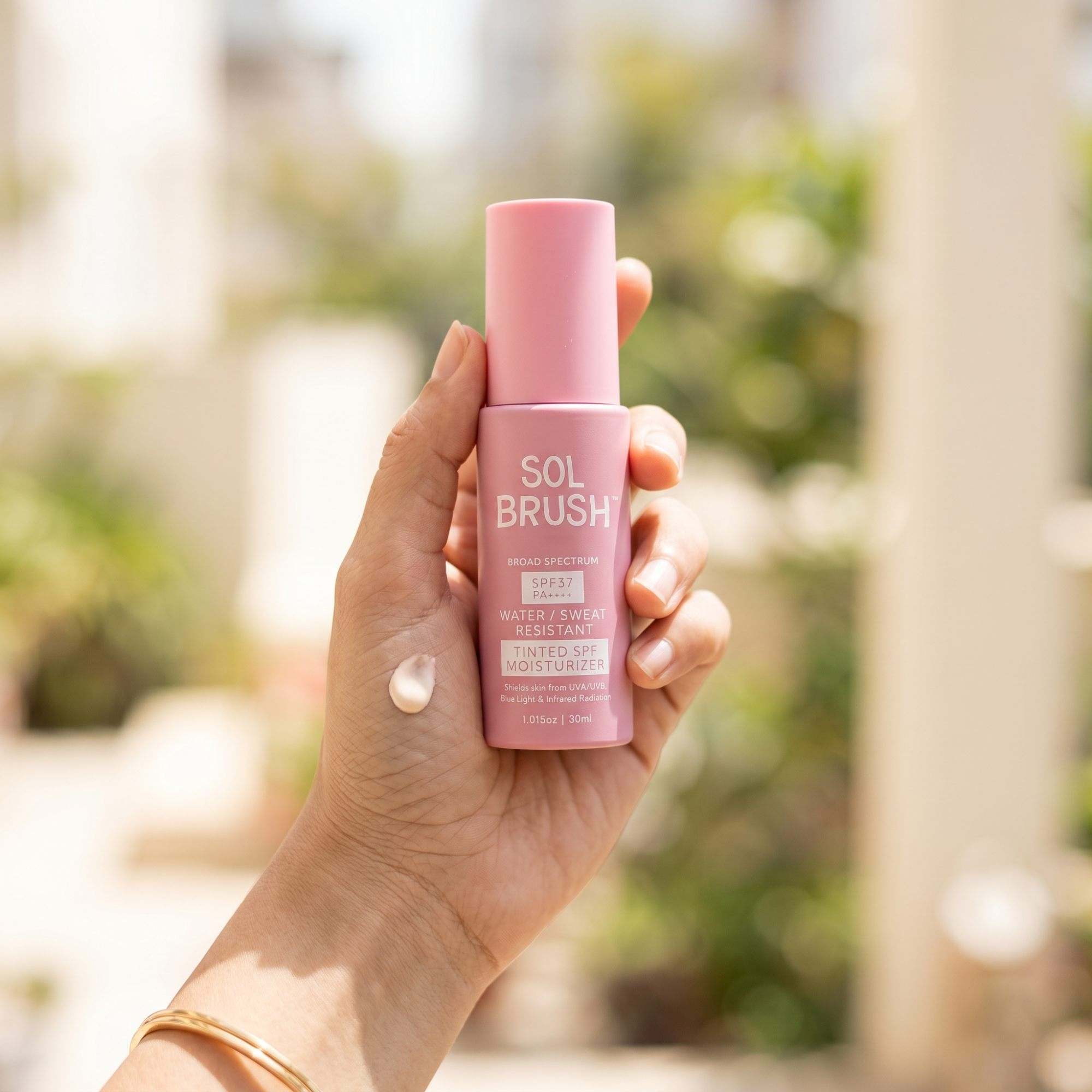 Hand holding the Tinted SPF Moisturizer bottle with a small drop of the tinted cream on the skin