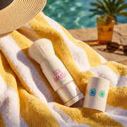 White Sol Brush powder sunscreen brush uncapped on a yellow striped towel by the pool