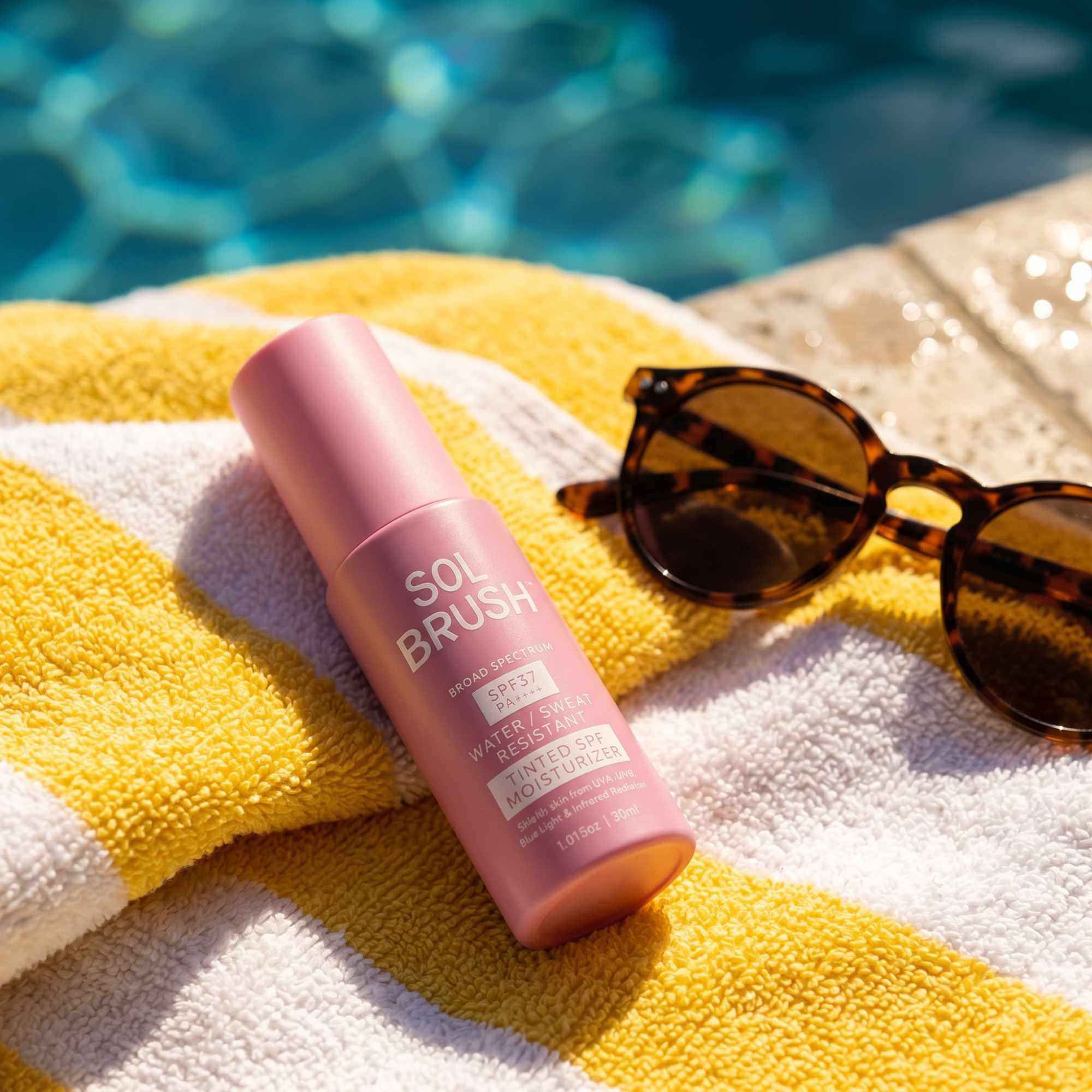 Tinted SPF Moisturizer Broad Spectrum SPF 37 lying on a yellow striped towel beside sunglasses at the pool